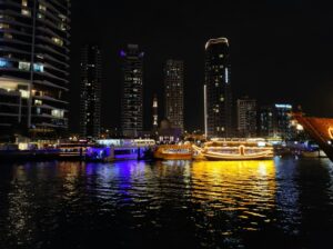 Illuminated yachts on a lively waterway in Dubai against a backdrop of skyscrapers at night.