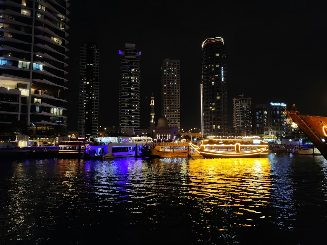 Illuminated yachts on a lively waterway in Dubai against a backdrop of skyscrapers at night.